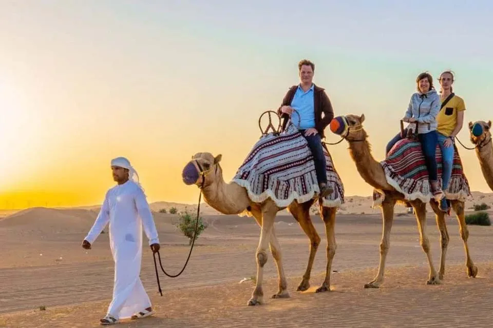 Tourists riding camels on a tranquil Morning Desert Safari in Dubai at sunrise